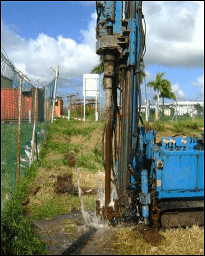 A blue mechanical drill drilling into watery ground.