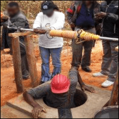 A worker wearing a hard hat entering the well.