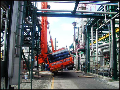 The orange crane balancing against metal work. The vehicle has been partially lifted off the ground to one side. 