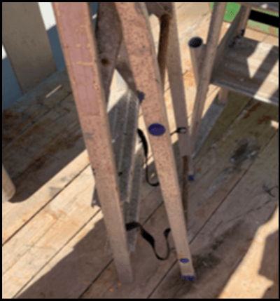 Een ingeklapte ladder met tekenen van corrosie en ontbrekende plastic steunen aan de onderkant 