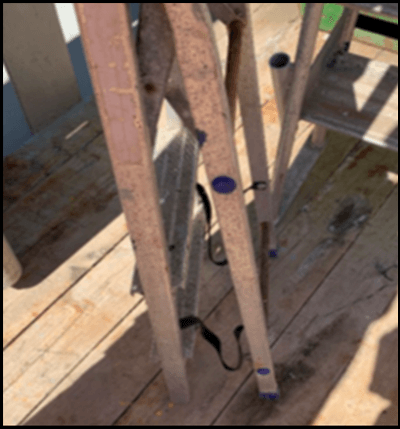 Uma escada dobrada com sinais de corrosão e suportes de plástico faltando na parte inferior 