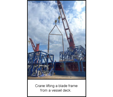 Crane lifting a blade frame from a vessel deck.