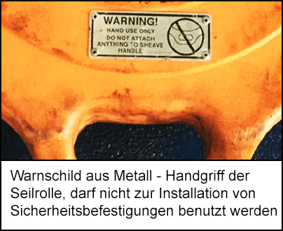 Ein Warnschild aus Metall am Handgriff der orangen Seilrolle