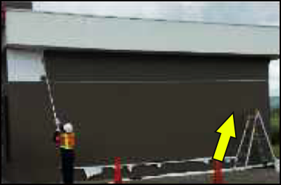 Un trabajador estaba pintando el muro exterior de una estación de servicio con una brocha extensible. El tubo de luz dañado está en la parte superior de la pared.