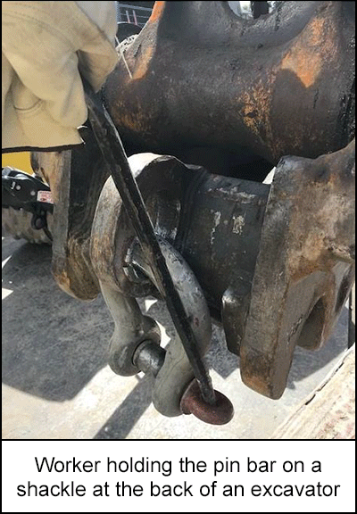 worker holding the pin bar on a shackle at the back of an excavator