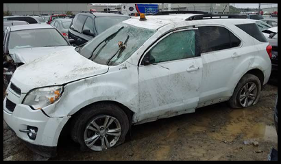 A white car with dents along the body of the car and smashed windows resulting from the vehicle rolling over. 