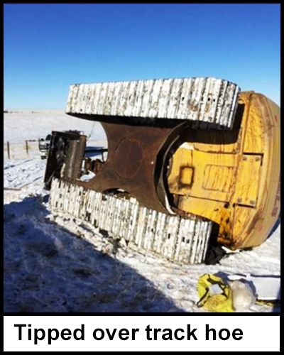 The tipped over yellow track hoe lying on its side in a filed covered with icy snow. 